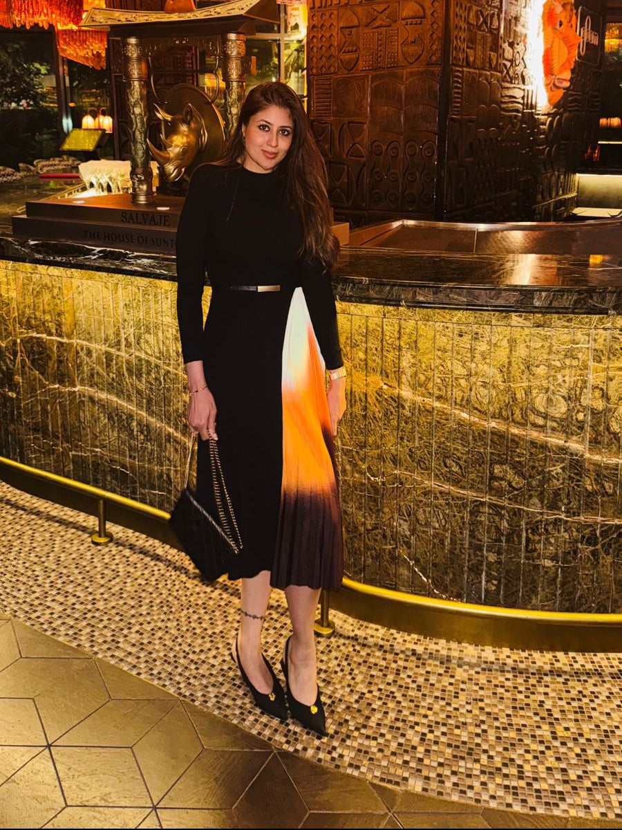 Woman in a black dress with gradient skirt standing in a luxurious interior setting.